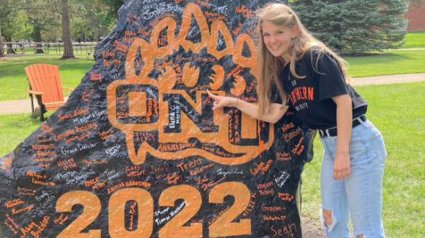 Young woman stands next to rock smiling. Rock says "ONU 2022" with signatures on it.