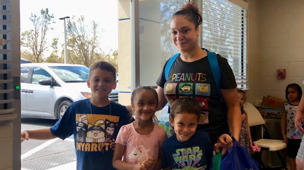 A family of four - one adult and three children - smiling at camera inside.