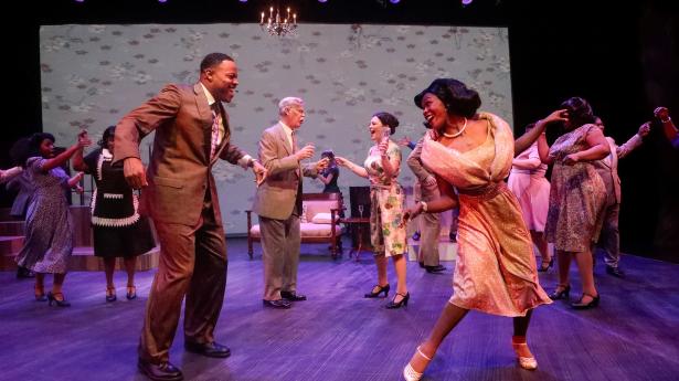 A man and a woman dance on stage with people dancing in the background. 